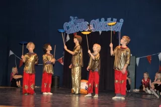 Vier kinderen met ronddraaiende bordjes op stokjes, op achtergrond logo Circus Okidoki